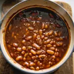 A bowl of homemade baked beans garnished with fresh parsley.