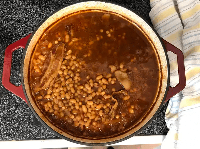 Delicious homemade baked beans in a serving dish, topped with crispy bacon and fresh herbs