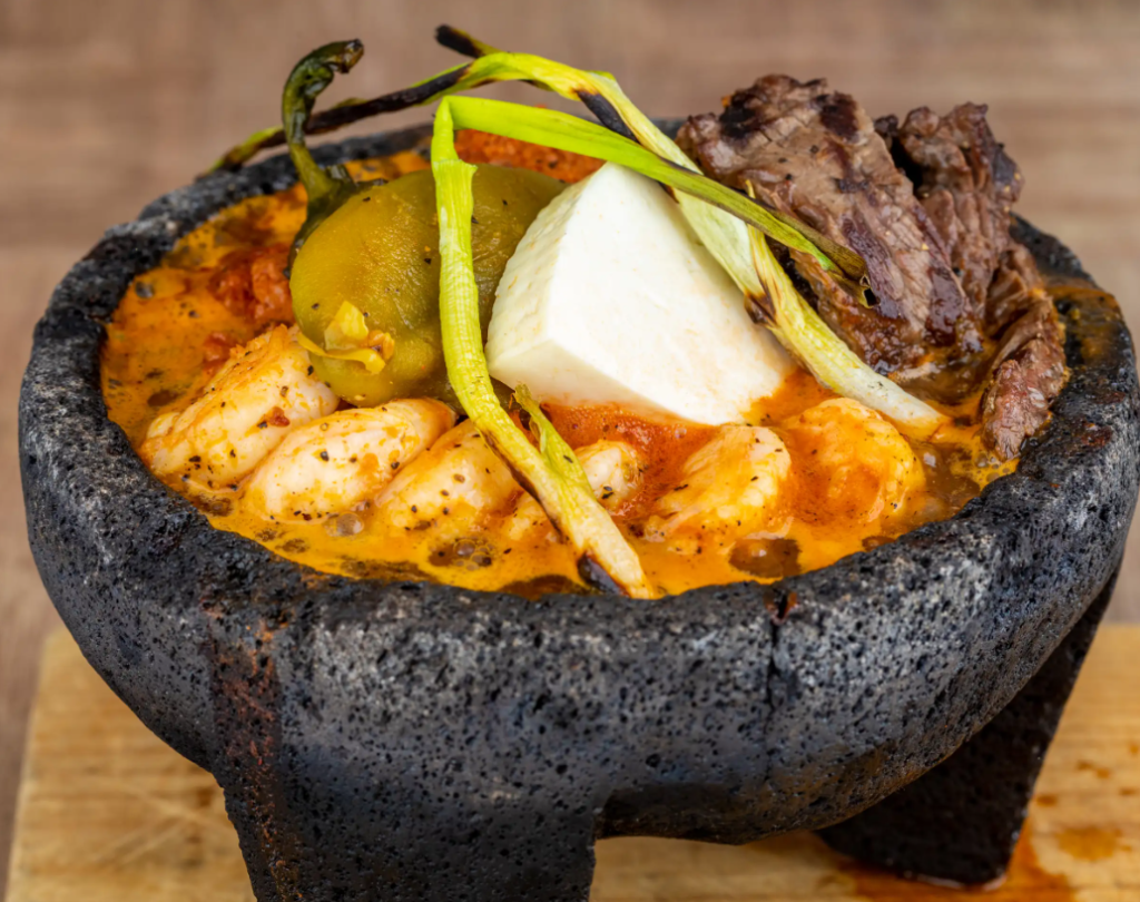Freshly prepared molcajete salsa with vibrant tomatoes, cilantro, and avocados in a traditional stone molcajete.