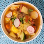 Delicious bowl of Caldo de Res, featuring tender beef chunks, corn, carrots, and potatoes in a savory broth garnished with cilantro.
