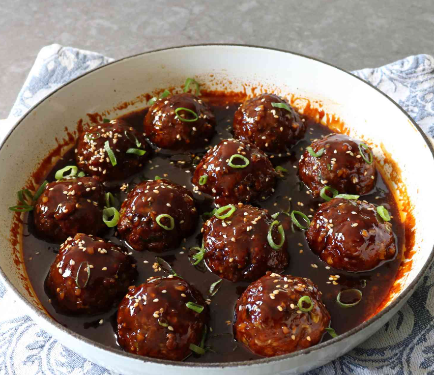 Plate of juicy barbecue meatballs garnished with fresh parsley on a rustic wooden table