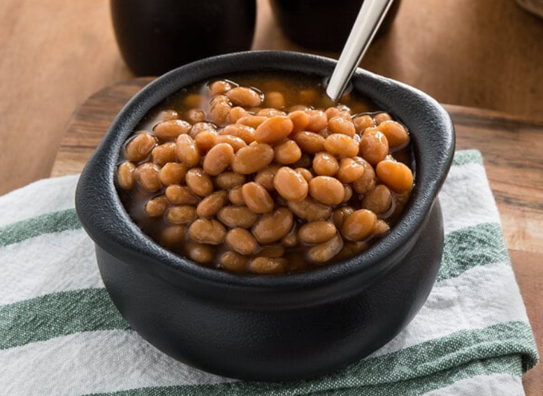 Bowl of Bush's Baked Beans garnished with fresh herbs, served on a rustic wooden table