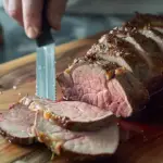 Sliced roast beef on a cutting board with herbs