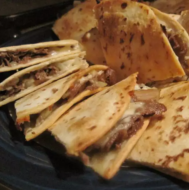 Freshly cooked steak quesadilla on a plate with melted cheese and vibrant garnishes