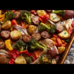 Alt text: "Colorful Italian sausage sheet pan recipe with roasted vegetables including red bell peppers, zucchini, and potatoes, garnished with fresh herbs."