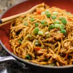 Alt text: "A vibrant plate of Spicy Peanut Chicken Noodles Recipe featuring tender chicken pieces, colorful vegetables, and a rich, creamy peanut sauce garnished with fresh cilantro and sliced red chili peppers."