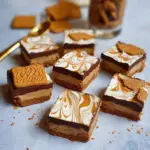 "Image of No-Bake Lotus Biscoff Cheesecake Bars Recipe featuring a creamy cheesecake layer topped with Biscoff cookie crumbs and a smooth Biscoff spread drizzle on a wooden table."